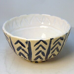 May include: A white ceramic bowl with a blue and white geometric pattern. The bowl has a scalloped rim and a slightly flared shape.