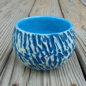May include: A small, round ceramic bowl with a blue and white speckled glaze. The bowl has a textured exterior with a pattern of blue lines.