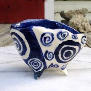 May include: A small, white ceramic bowl with blue and white swirl designs. The bowl has three legs and is perfect for holding small items.