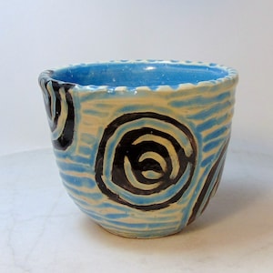 May include: A small, white ceramic bowl with blue and black swirling patterns. The bowl has a slightly uneven rim and a textured surface.