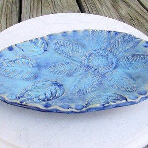 May include: A blue ceramic dish with a leaf design. The dish is oval shaped and has a textured surface.