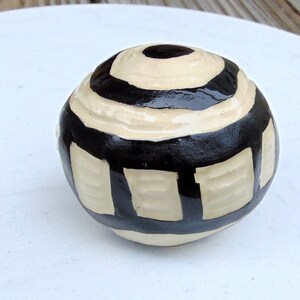 May include: A white ceramic sphere with black stripes and geometric patterns.