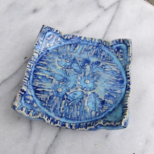 May include: A blue and white ceramic dish with a decorative design. The dish has a scalloped edge and a raised center.