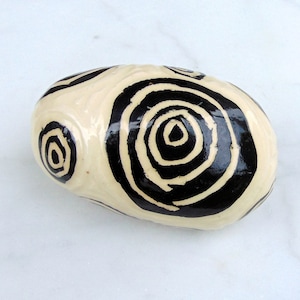 May include: A white ceramic egg with black concentric circles painted on the surface.