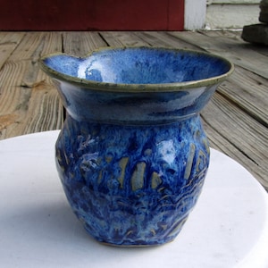 May include: A blue and brown ceramic vase with a textured surface. The vase has a wide mouth and a rounded body.