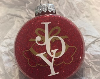 May include: Red glitter Christmas ornament with a white "JOY" design and gold bells.