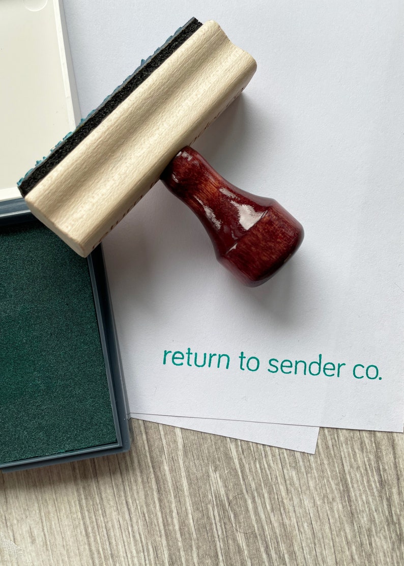 May include: A wooden stamp with a dark red handle and the text "return to sender co." printed in green. The stamp is next to a green ink pad.