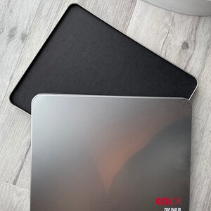 May include: A silver rectangular ink pad with rounded corners, displaying the text "COLOR TOP PAD" in red. The pad is open, revealing a black ink surface. The pad is on a light grey wooden surface.