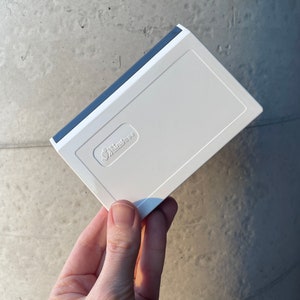 May include: A white rectangular product with a blue trim. The product features the text "Spiritless" in a recessed area. The item is held in a hand against a grey background.