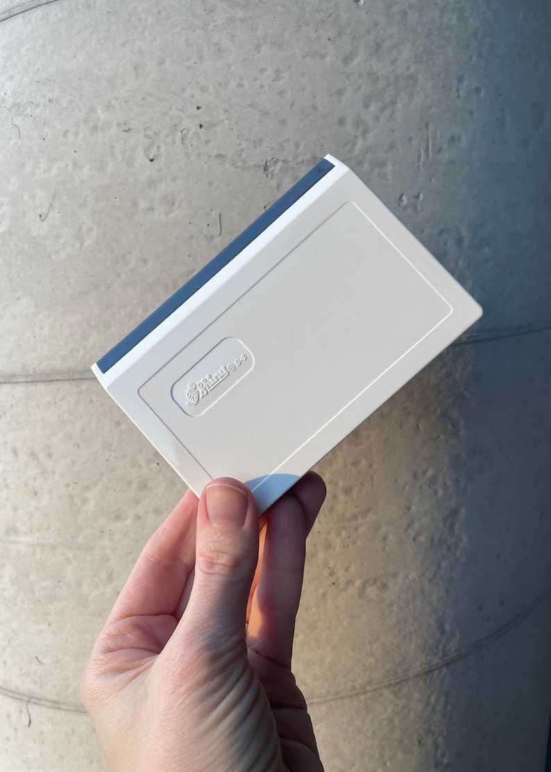 May include: A white rectangular product with a blue trim. The product features the text "Spiritless" in a recessed area. The item is held in a hand against a grey background.
