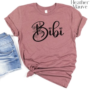 May include: A heather mauve t-shirt with the word "Bibi" in black script with a floral design behind the "B".