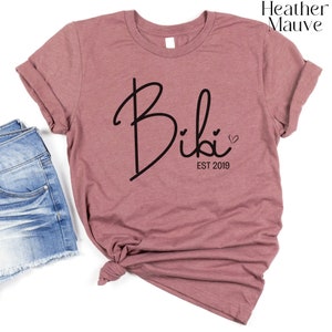 May include: Heather mauve t-shirt with the text "Bibi Est 2019" in black script with a small heart.