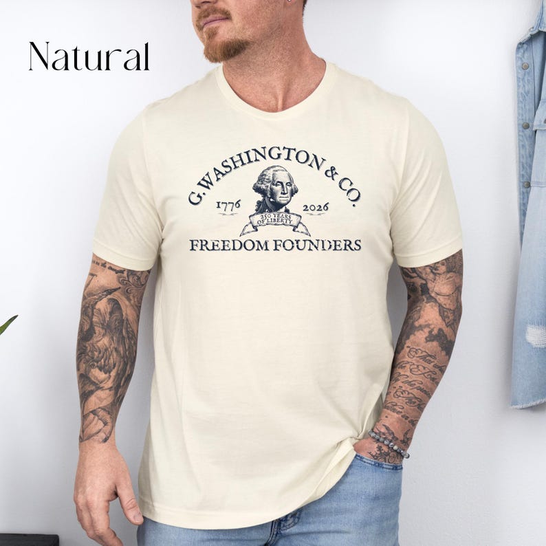 May include: Cream-colored t-shirt with a crew neck featuring a vintage-style graphic. The graphic includes the text "G. Washington & Co." above an image of George Washington, with the years 1776 and 2026, and the words "Freedom Founders".