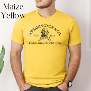 May include: Maize yellow t-shirt with the text "G. Washington & Co. 1776-2026 Freedom Founders" in black. The shirt features a portrait of George Washington. The words "Maize Yellow" are in the upper left corner.