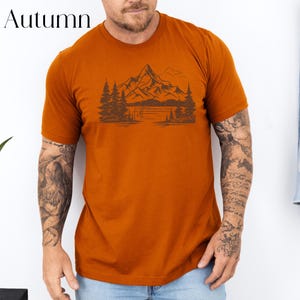 May include: A rust-colored t-shirt with a graphic of a mountain range and a lake. The graphic is in black and white.