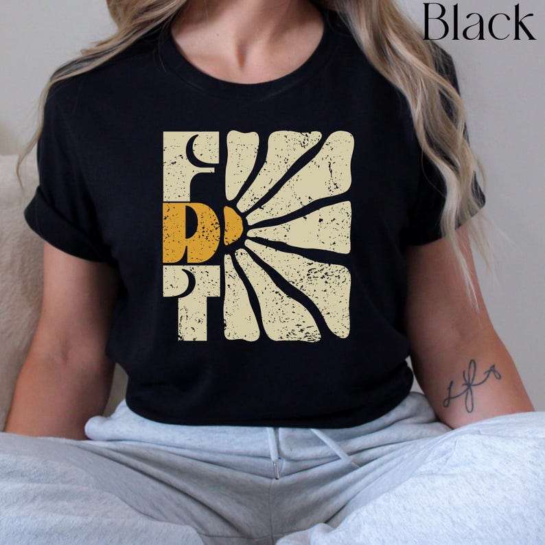 May include: Black t-shirt featuring a vintage-style graphic of a sun with rays and the word "First" in yellow lettering.