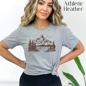 May include: A gray t-shirt with a brown graphic of a mountain range and a lake. The text "Athletic Heather" is printed in black at the top of the image.