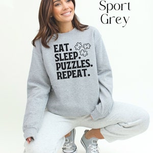 May include: A gray sweatshirt with the text "Eat. Sleep. Puzzles. Repeat." and a graphic of three puzzle pieces.