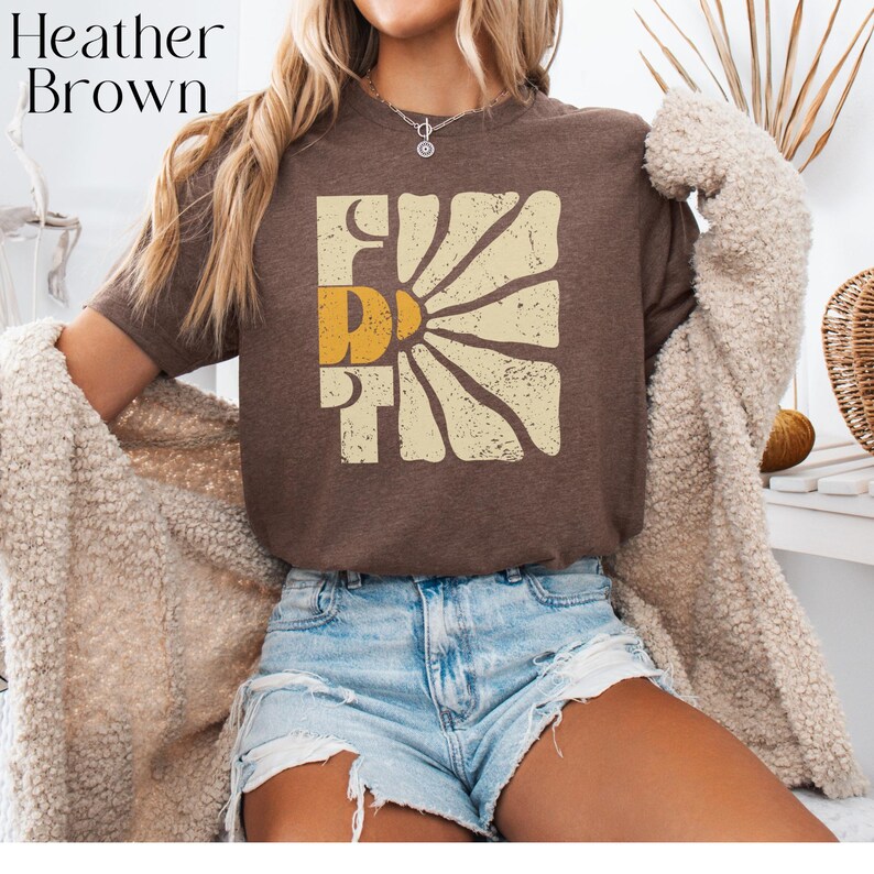 May include: A brown t-shirt with a vintage-style graphic of a sun with the word "First" in a yellow and cream colour scheme.