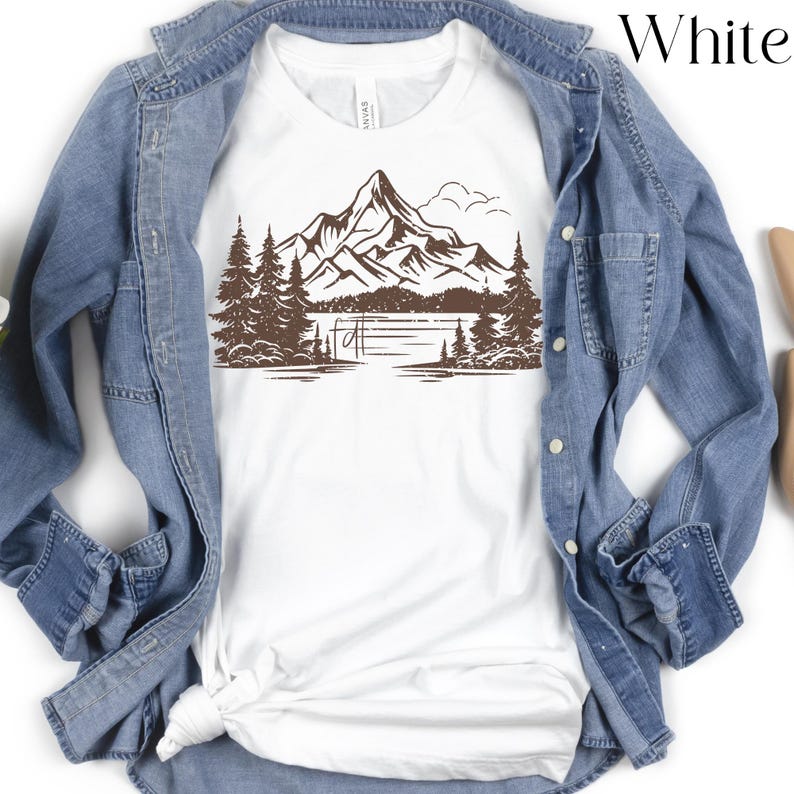 May include: White t-shirt with a brown graphic of a mountain range, lake, and trees.