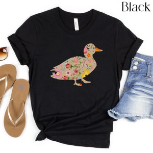 Peut inclure: T-shirt noir avec un motif de silhouette de canard floral. Le canard est d&eacute;limit&eacute; en noir et rempli d'un motif de fleurs color&eacute;es.