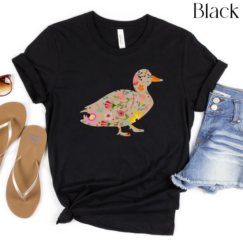 Peut inclure: T-shirt noir avec un motif de silhouette de canard floral. Le canard est d&eacute;limit&eacute; en noir et rempli d'un motif de fleurs color&eacute;es.