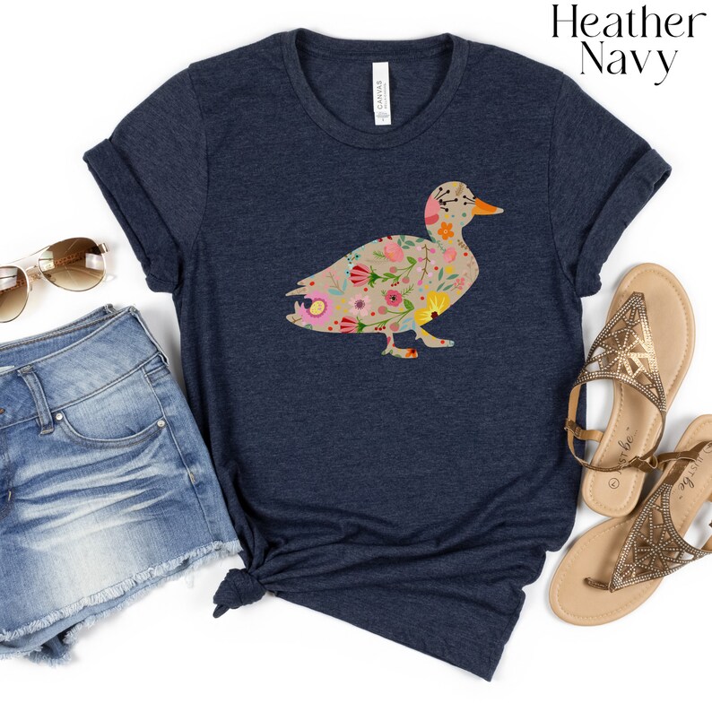 Peut inclure: Un t-shirt bleu marine chin&eacute; avec un motif de silhouette de canard floral. Le canard est rempli de fleurs et de feuilles color&eacute;es.