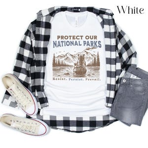May include: White t-shirt with a brown bear and a smaller bear cub standing in front of a mountain range with the text "Protect Our National Parks" and "Resist. Persist. Prevail."