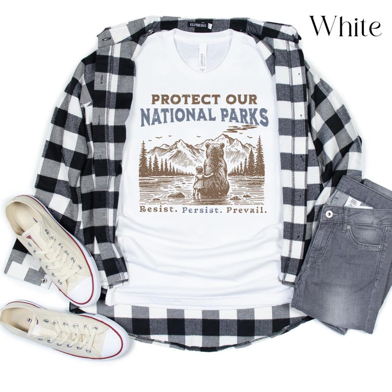 May include: White t-shirt with a brown bear and a smaller bear cub standing in front of a mountain range with the text "Protect Our National Parks" and "Resist. Persist. Prevail."