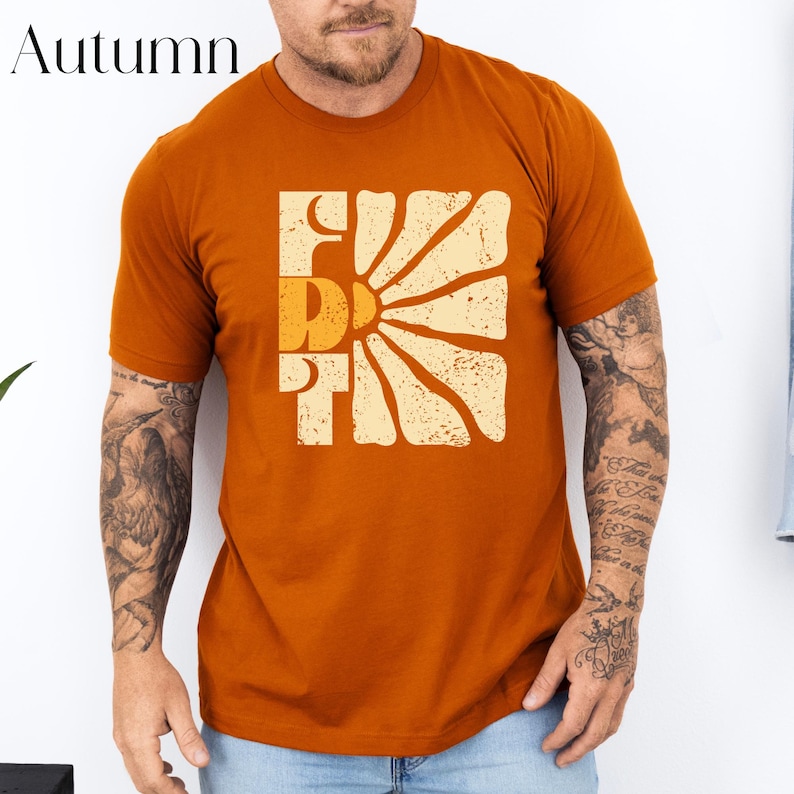 May include: A rust-coloured t-shirt with a retro sunburst graphic and the word "Friday" in a vintage font.