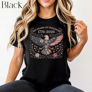 May include: Black t-shirt featuring a patriotic design. The graphic includes an eagle with wings in the colors of the American flag, surrounded by floral elements. The text "250 YEARS OF FREEDOM 1776-2026" is arched above the eagle.