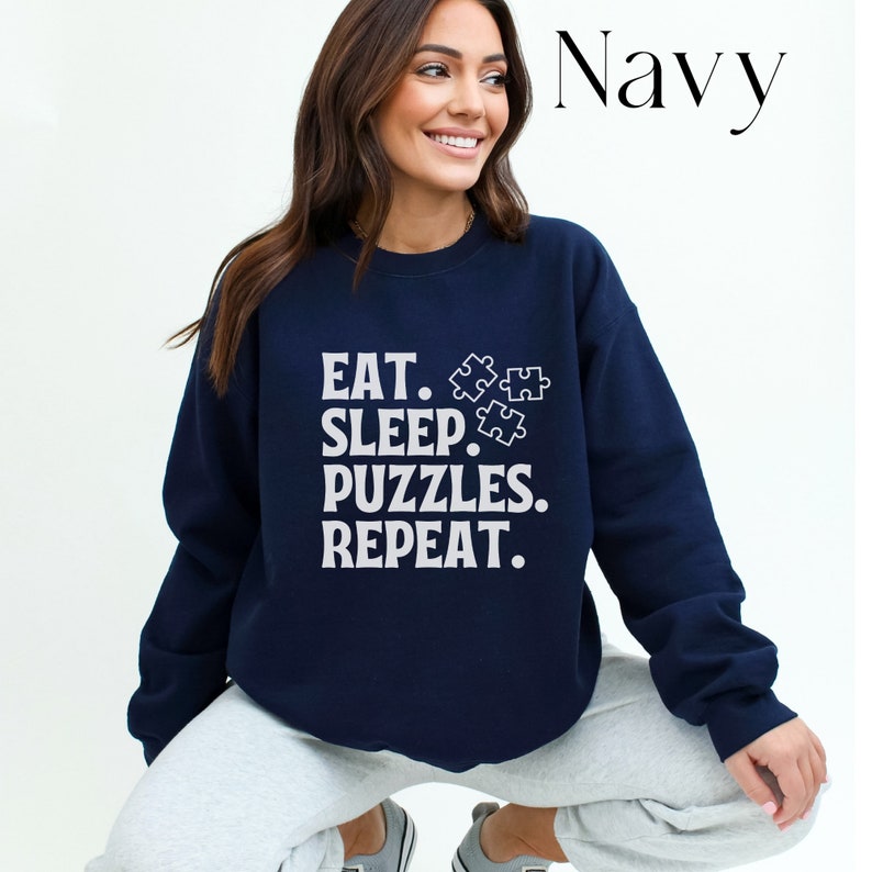 May include: A navy blue sweatshirt with a white graphic that says "Eat. Sleep. Puzzles. Repeat." and features three puzzle pieces.