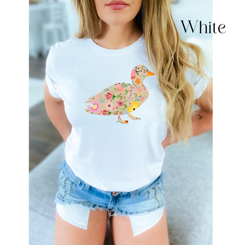Peut inclure: T-shirt blanc avec un motif de canard floral. Le canard est d&eacute;limit&eacute; par un contour brun et rempli de fleurs color&eacute;es.