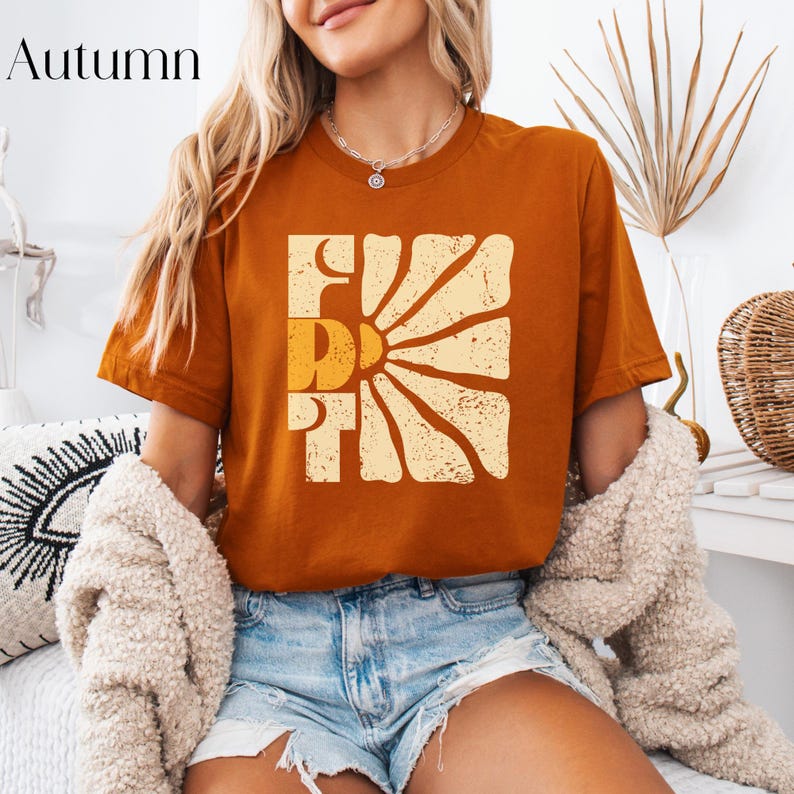 May include: A burnt orange t-shirt with a graphic of a sun with the word "First" in a retro font.