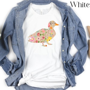 Peut inclure: T-shirt blanc avec une silhouette de canard &agrave; motif floral. Le canard est d&eacute;limit&eacute; par un contour brun et rempli de fleurs roses, jaunes et vertes.