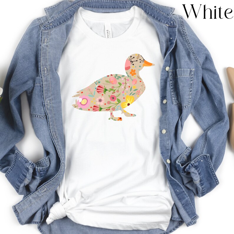 Peut inclure: T-shirt blanc avec une silhouette de canard &agrave; motif floral. Le canard est d&eacute;limit&eacute; par un contour brun et rempli de fleurs roses, jaunes et vertes.