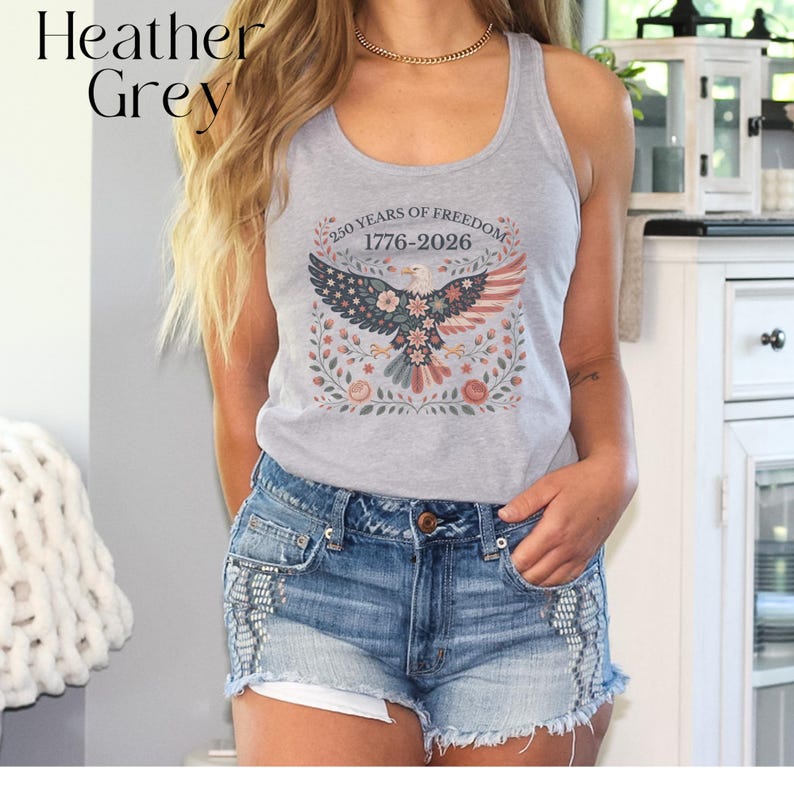 May include: Heather grey tank top with a graphic of an eagle with the American flag design and the text "250 YEARS OF FREEDOM 1776-2026". The tank top is paired with denim shorts.