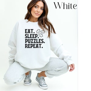 May include: White sweatshirt with the text "EAT. SLEEP. PUZZLES. REPEAT." and a graphic of three puzzle pieces.