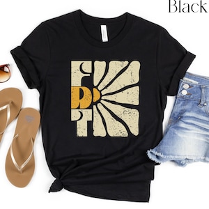 May include: Black t-shirt featuring a vintage-style graphic of a sun with the word "FUN" in a yellow and orange colour scheme.