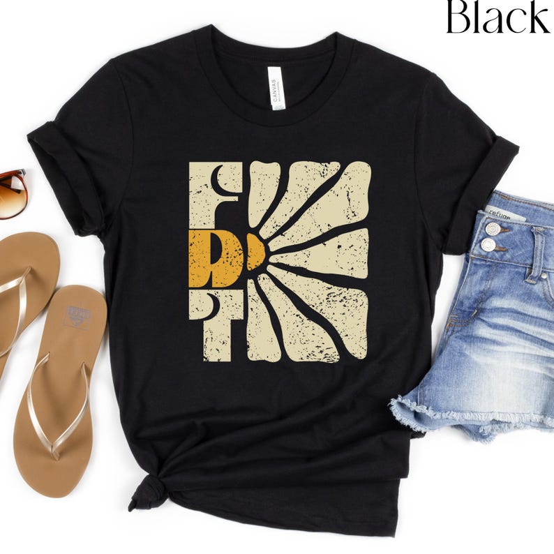 May include: Black t-shirt featuring a vintage-style graphic of a sun with the word "FUN" in a yellow and orange colour scheme.