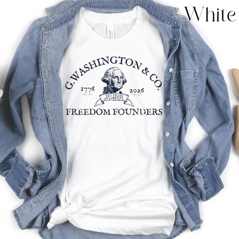 May include: White t-shirt with a navy blue graphic featuring an illustration of George Washington and the text "G. Washington & Co. 1776-2026 Freedom Founders". The shirt is layered under a light blue denim jacket.