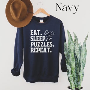May include: Navy blue sweatshirt with white text that reads "Eat. Sleep. Puzzles. Repeat." and three white puzzle piece icons.