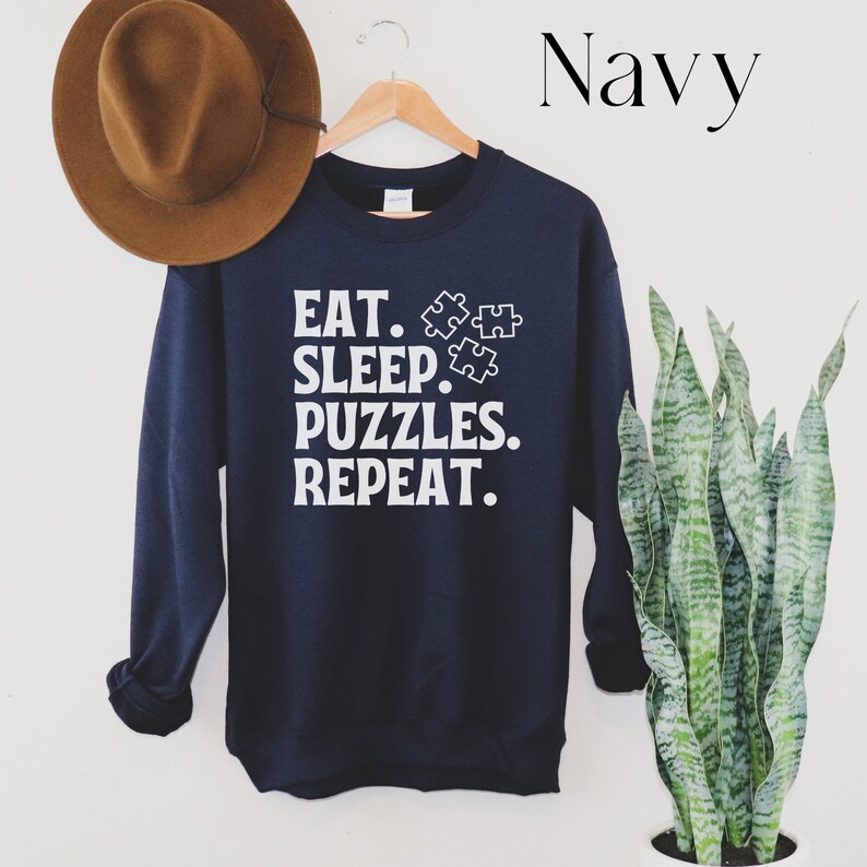 May include: Navy blue sweatshirt with white text that reads "Eat. Sleep. Puzzles. Repeat." and three white puzzle piece icons.