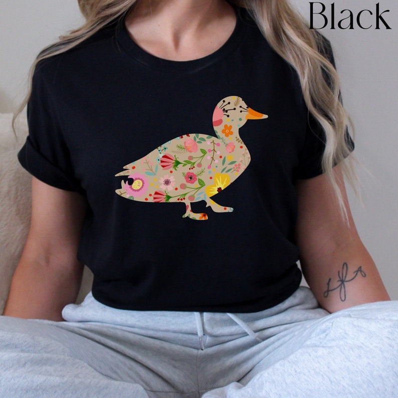 Peut inclure: Un t-shirt noir avec un motif de silhouette de canard floral. Le canard est rempli de fleurs et de feuilles color&eacute;es.