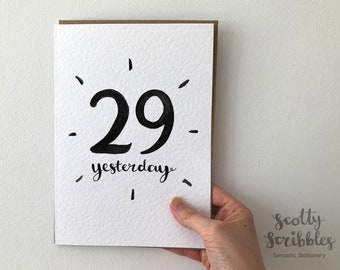 May include: A white card with black ink reads "29 yesterday" with a few black dashes around the number. The card is held in a hand against a white background. The bottom of the card has the text "scotty scribbles sarcastic stationery".