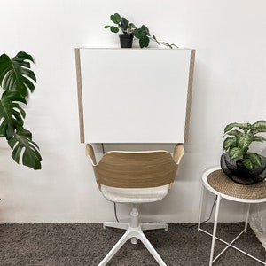 Puede incluir: Un escritorio blanco montado en la pared con paneles laterales de madera clara sobre una silla con respaldo curvo de madera clara, asiento tapizado en gris claro y base blanca de cinco puntas con ruedas para un espacio de trabajo.