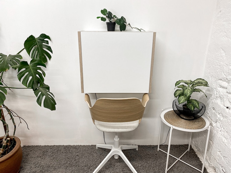 Puede incluir: Un escritorio blanco montado en la pared con paneles laterales de madera clara sobre una silla con respaldo curvo de madera clara, asiento tapizado en gris claro y base blanca de cinco puntas con ruedas para un espacio de trabajo.