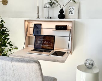 May include: A wall-mounted light wood drop-leaf desk with integrated LED lighting. The desk features a fold-down work surface, internal shelving, and metal support struts. A laptop with the text BITMAN WOOD is open on the desk surface.