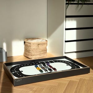 May include: A rectangular wooden tray with a black frame and a white base featuring a printed black racetrack design. The tray includes several small toy cars arranged in the centre and the text BITMAN WOOD printed in the bottom left corner.