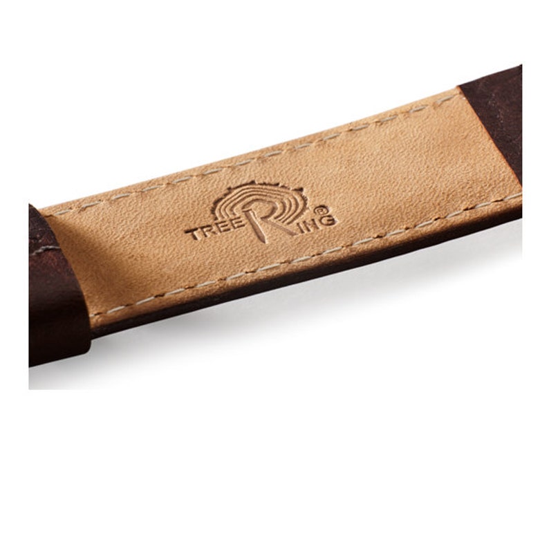 May include: Close-up of a brown leather watch strap with the Tree Ring logo embossed in the center. The logo features a stylized tree ring design with the word "Tree Ring" written above and below the design.